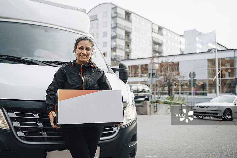 在城市里，一名微笑的女工背着一个箱子，站在货车旁边图片素材