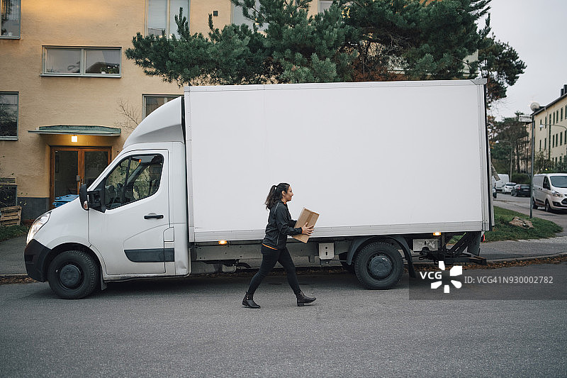 在城市的街道上，女工人背着箱子，走在送货车上图片素材