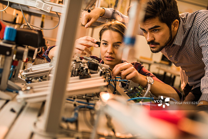 两个工程专业的学生在实验室里研究机器的电气元件。图片素材