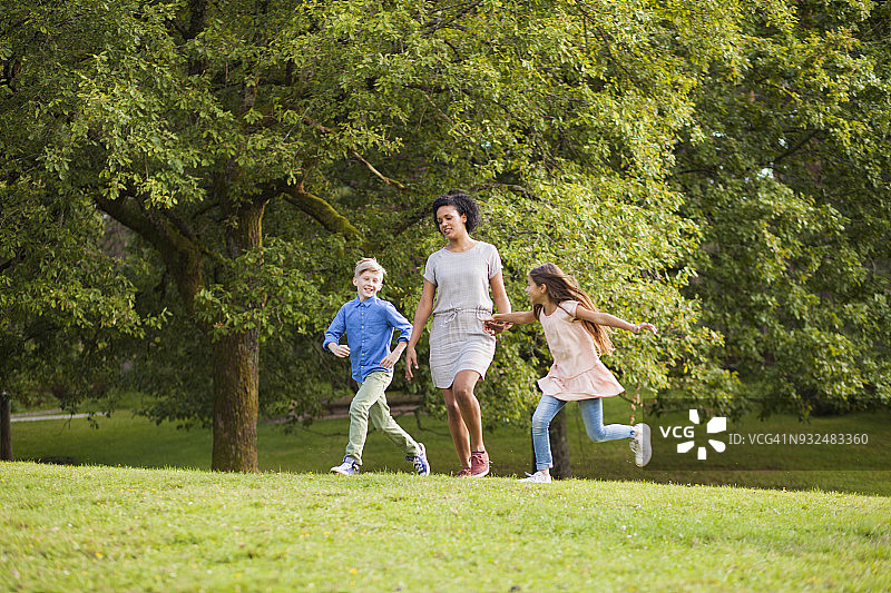年轻女子和两个孩子手牵着手在公园里跑步图片素材
