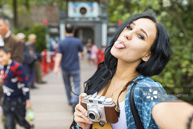 越南，河内，年轻女子拿着老式相机伸着舌头图片素材