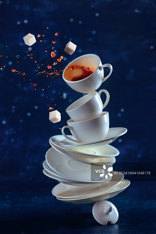 一叠摆置在桌上的白瓷咖啡杯。动态饮料摄影与咖啡溅在一个黑暗的背景。图片素材