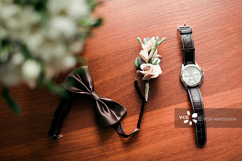 新娘花束，巧克力色的蝴蝶，优雅的钮扣和一个男士手表放在木桌上图片素材