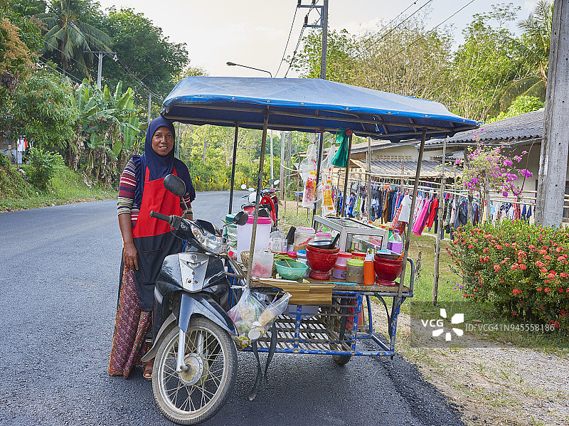 一位戴着头巾的女士在她的摩托车食品车旁摆姿势图片素材
