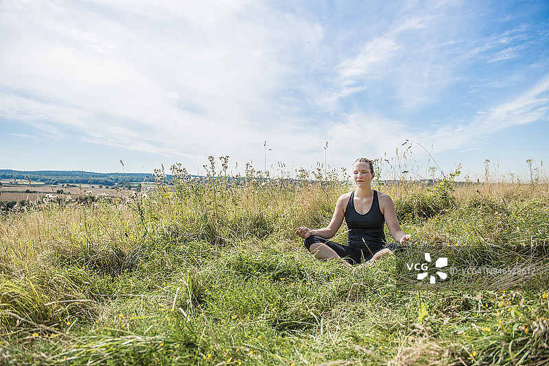 一个女人在外面的草地上享受阳光，同时练习瑜伽图片素材
