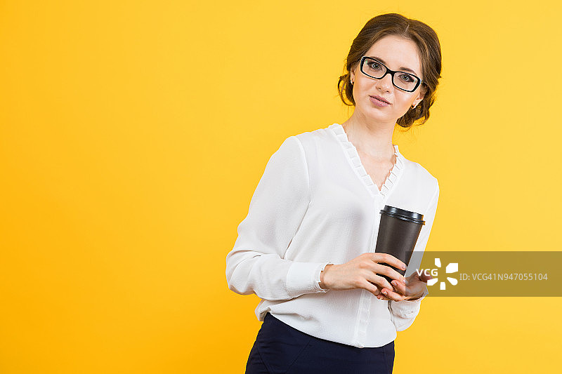 肖像自信美丽的年轻优雅的商务女人拿着一杯咖啡在她的手在黄色的背景图片素材