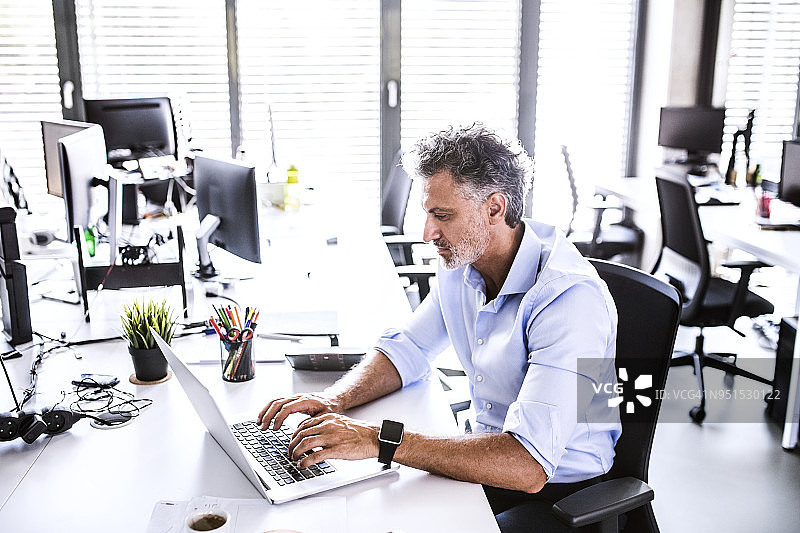 一个成熟的商人坐在办公室的办公桌前使用笔记本电脑图片素材