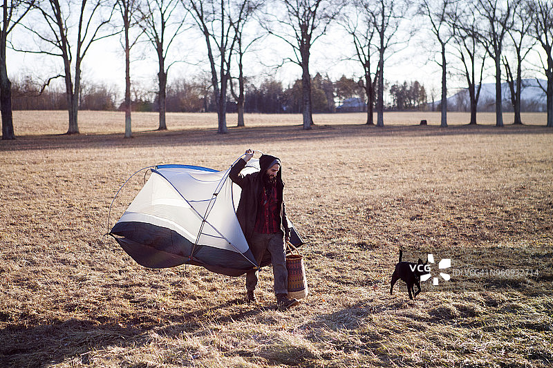 一个人带着便携式帐篷，带着狗在田野上散步图片素材
