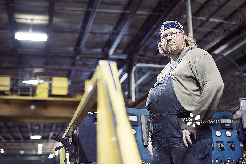 低角度的蓝领工人穿着围嘴工作服和头巾，而工作在钢铁工业图片素材