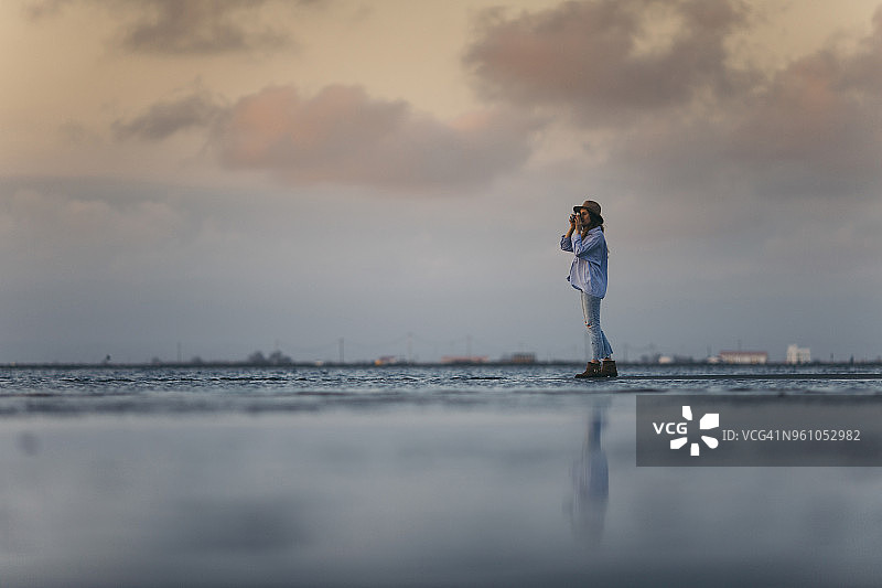 一名女子站在海滩上拍摄日落时分的阴天图片素材