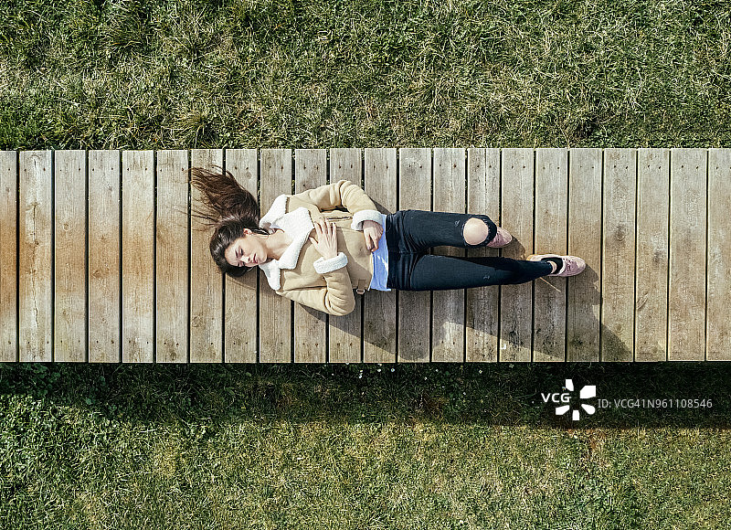 一个年轻女子躺在木板路上的俯视图图片素材