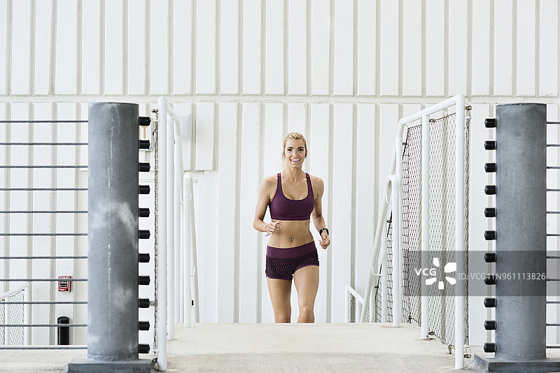 微笑的女运动员在停车场的台阶上跑步的肖像图片素材