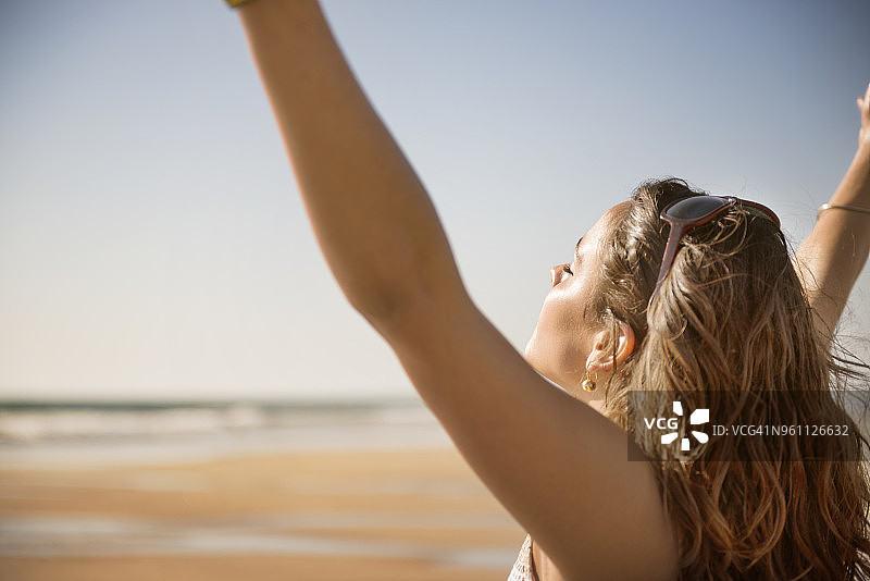 无忧无虑的女人在海滩上举起手臂的侧视图图片素材