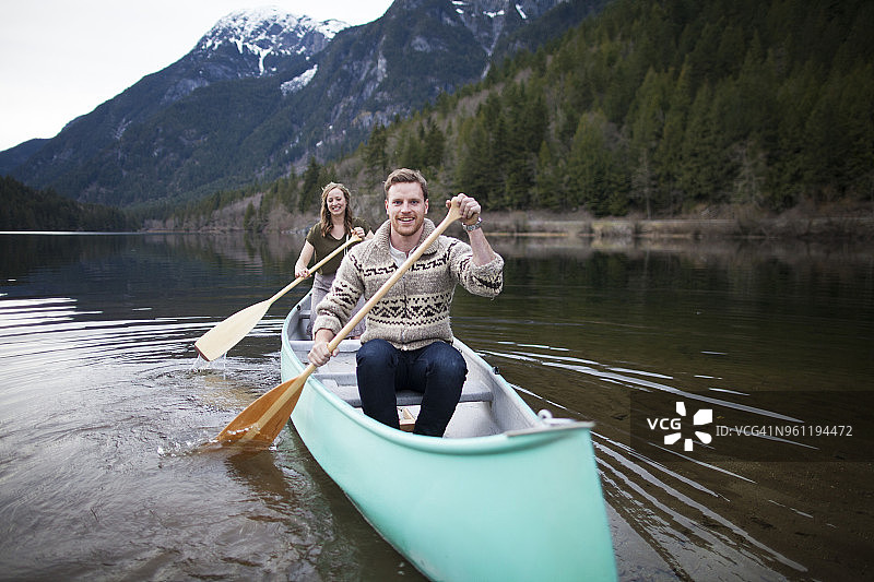 一对快乐的年轻夫妇在湖上对着山划独木舟图片素材