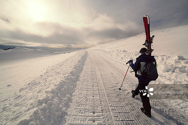 在雪地上行走时背着滑雪板的人的后视图图片素材