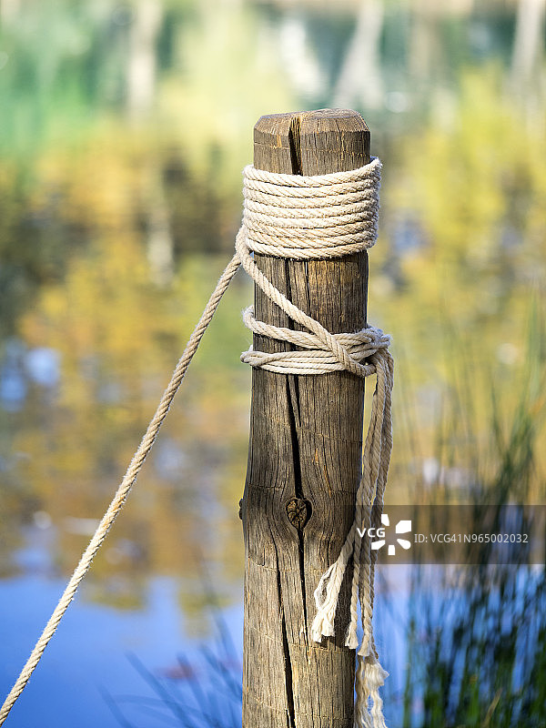 一根绑着绳子的木桩和结挂在湖边，与秋天树叶的颜色相辉映。图片素材