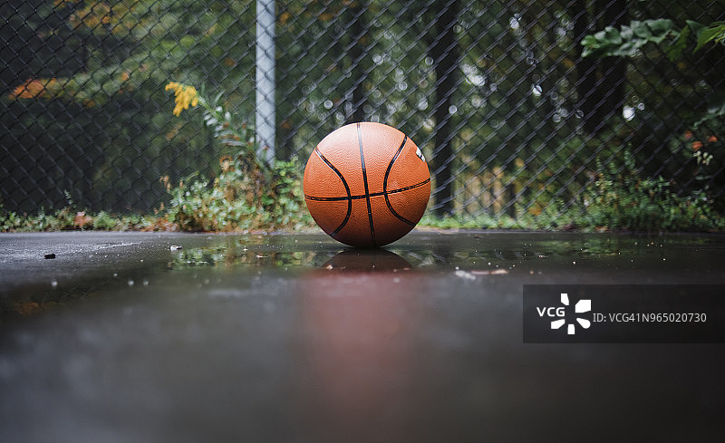 特写球在潮湿的篮球场上对着铁链围栏图片素材