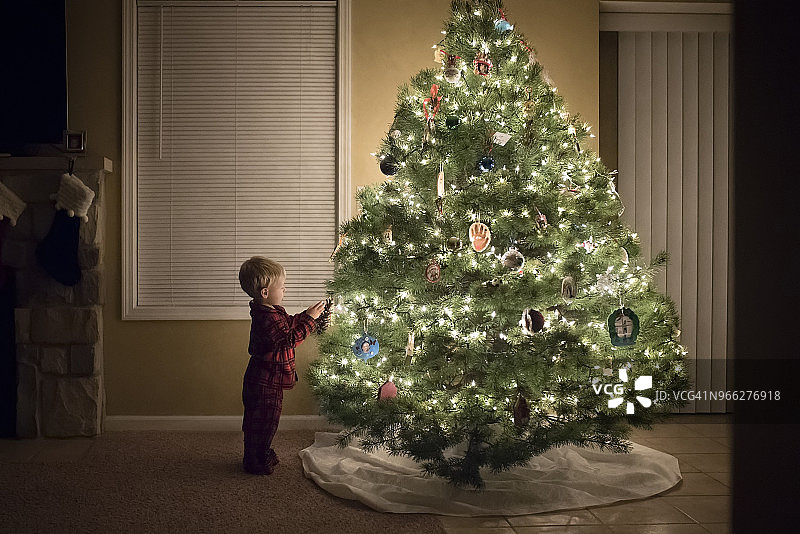 男孩站在家里的圣诞树旁的侧视图图片素材