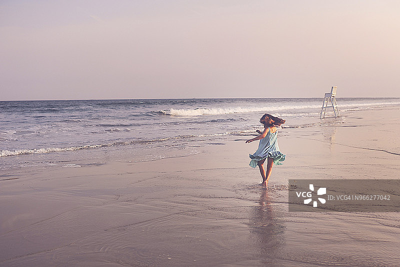 后视图的快乐女孩在海滩上玩的天空在日落图片素材