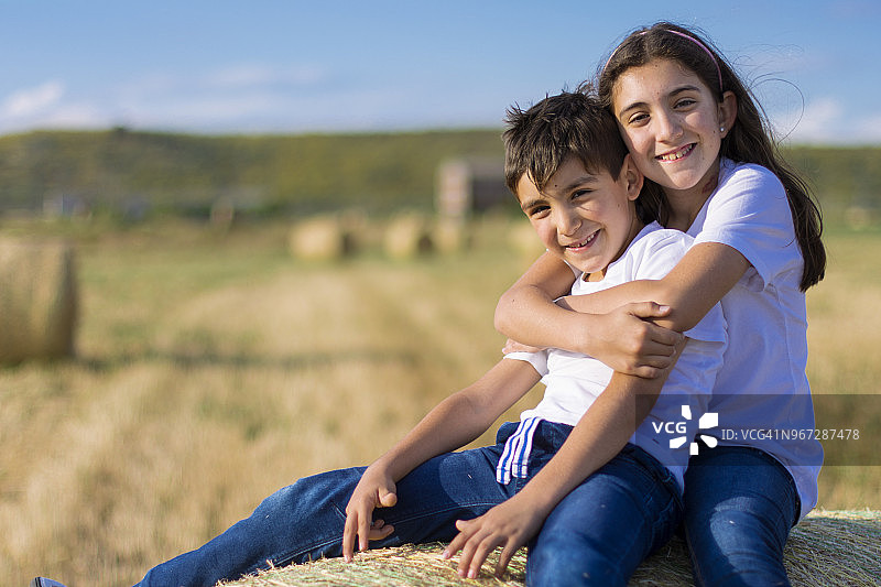 女孩坐在干草捆上拥抱她的弟弟图片素材