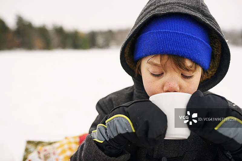 男孩站在雪地里喝热巧克力图片素材