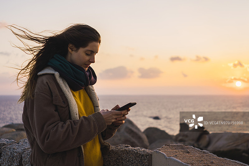 意大利撒丁岛，日落时分，一名女子在海边使用手机图片素材