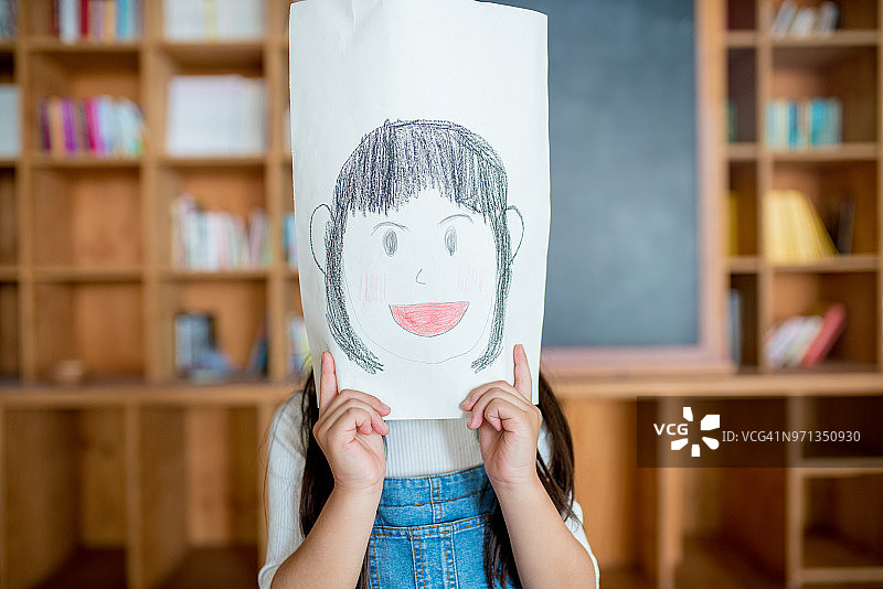 一个小女孩拿着一幅自画像挡在面前图片素材