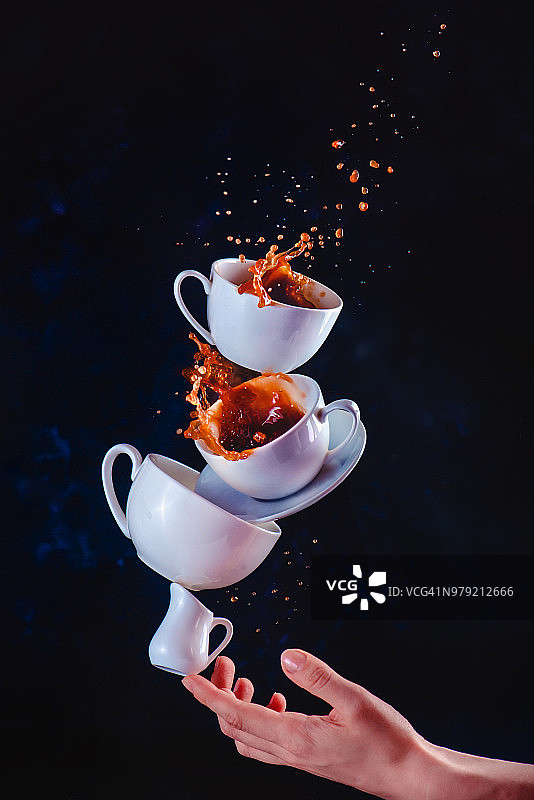 咖啡杯堆叠与动态喷溅平衡在一个指尖。运动中的高速食物摄影。深色背景和拷贝空间图片素材