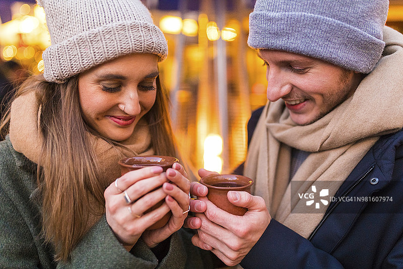 一对快乐的年轻夫妇在圣诞市场上喝着热红酒图片素材