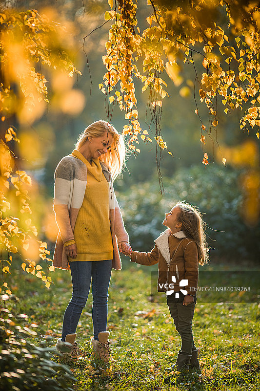 长长的快乐的单身母亲在秋日对她的小女儿说话。图片素材