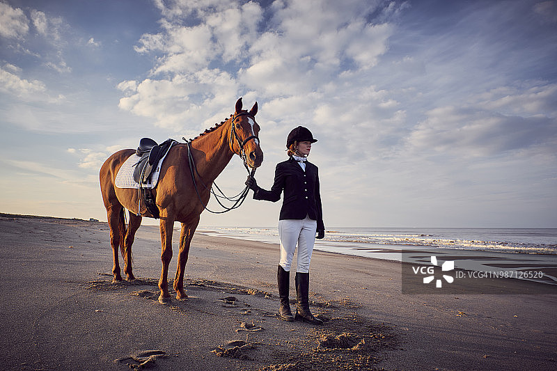一个年轻的女人和她的马站在海滩上图片素材