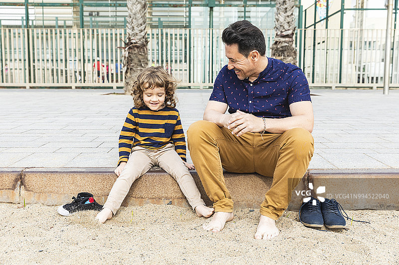 西班牙，巴塞罗那，父子俩光着脚坐在海边图片素材
