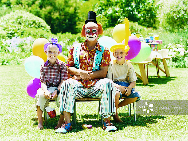 小丑和两个小男孩坐在花园里的椅子上图片素材