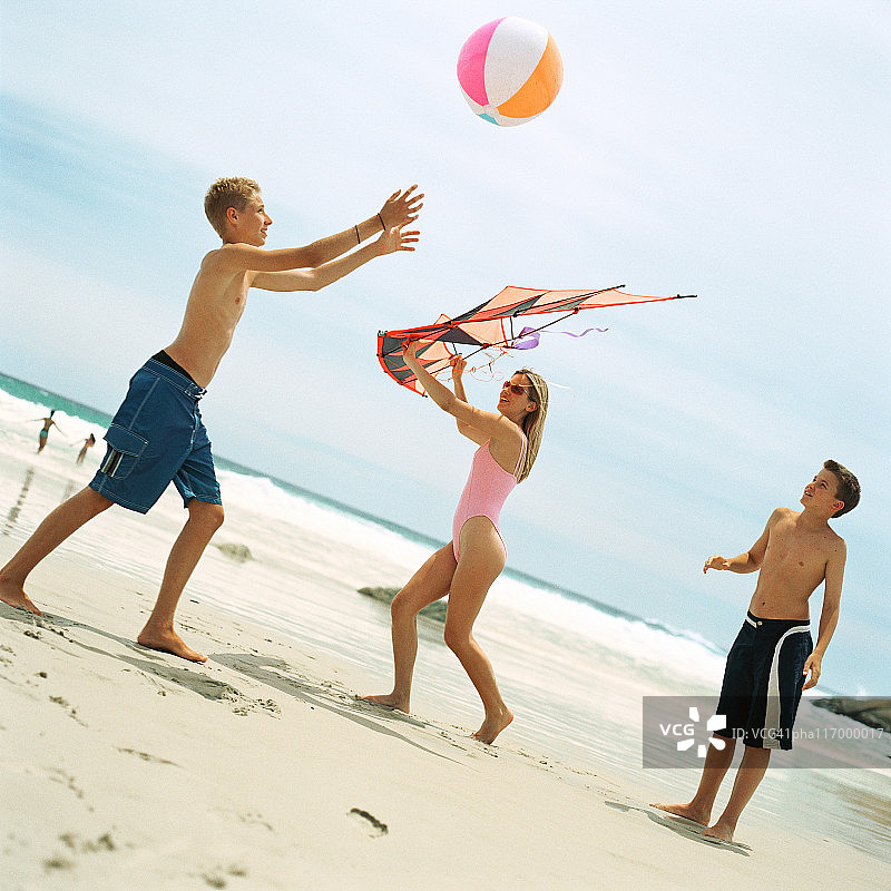 两个十几岁的男孩在玩沙滩球，女孩拿着风筝图片素材