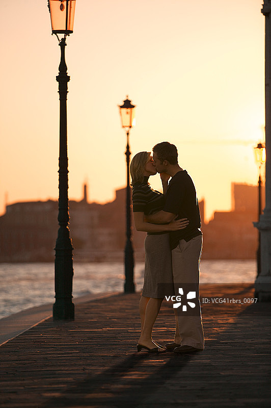 在日落时分，一对年轻的成年夫妇在码头上拥抱亲吻图片素材