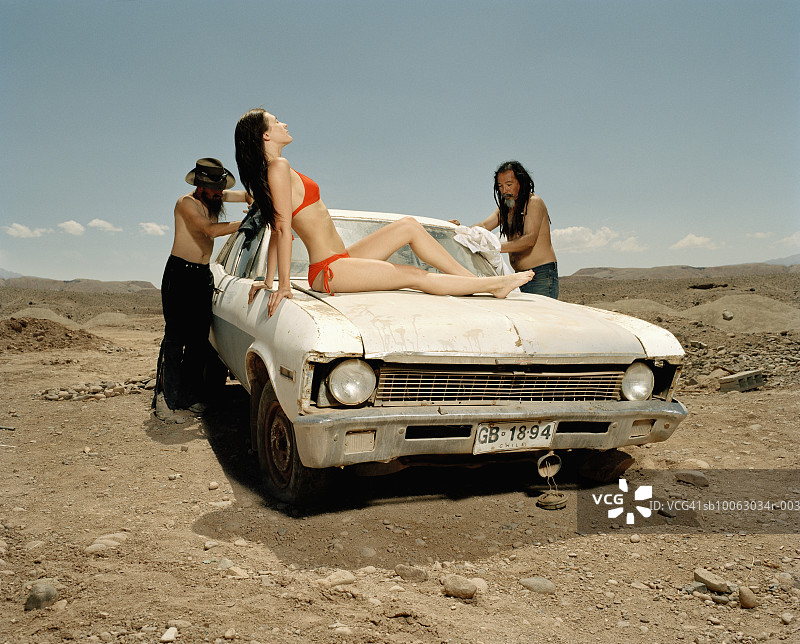 一个年轻女人躺在汽车上，被两个男人在沙漠里清洗图片素材
