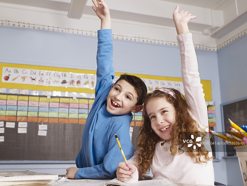 男孩和女孩(10-11)坐在教室里，举起手臂图片素材