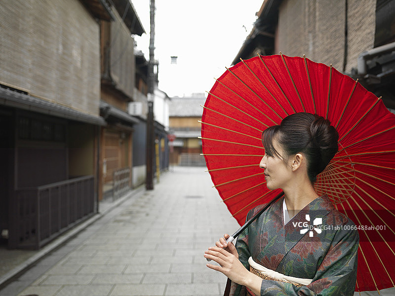 日本，京都，祗园，穿着和服的女人拿着红色油纸伞在街上图片素材