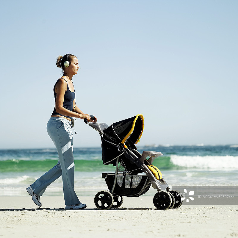 一个女人推着婴儿车在海滩上的侧视图图片素材