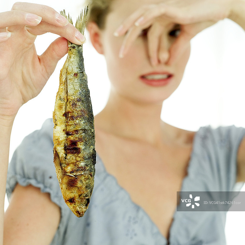 特写的女人拿着一条炸鱼和拿着她的鼻子图片素材