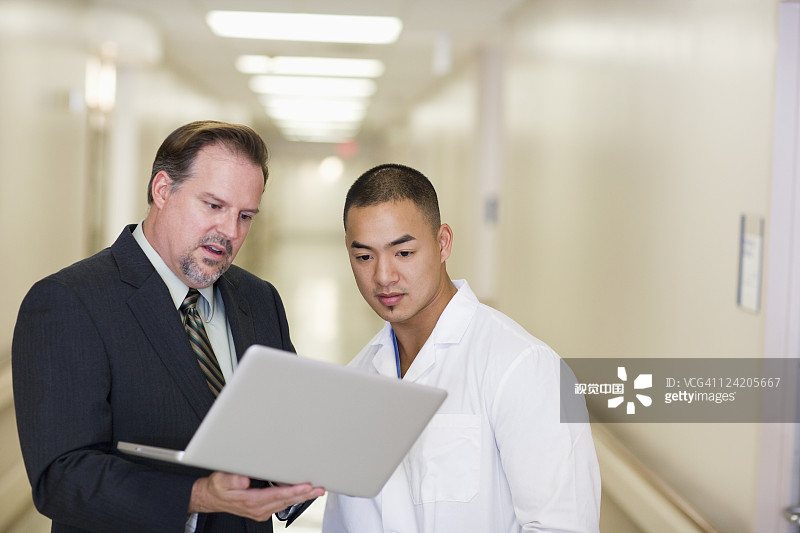 商人和医生在医院走廊里看笔记本电脑图片素材