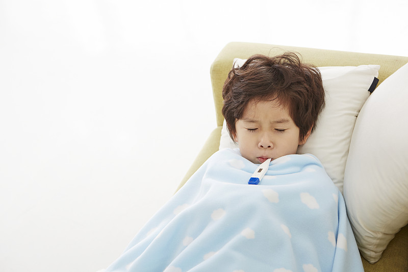 小男孩盖着毯子躺在沙发上生病的照片摄影图片