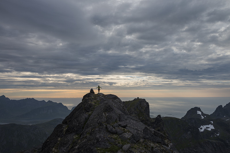 远处的女性徒步者在stjernind山顶日落，Flakstadoya Flakstadoya社区的最高峰Flakstadoya，罗浮敦群岛，挪威图片素材