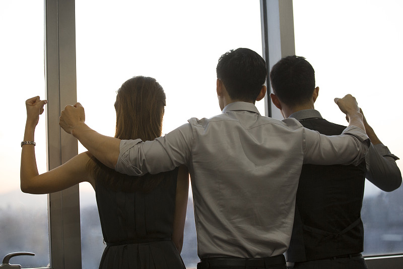 三个青年商务男女搂着肩膀站在公司会议室窗前一起看向窗外风景加油庆祝胜利图片下载
