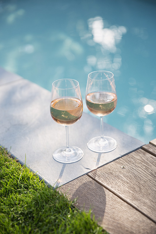 在阳光明媚，宁静的夏日泳池边品尝玫瑰酒图片下载