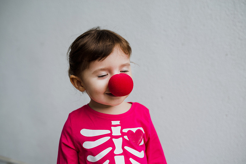 万圣节的宝贝女孩穿着骷髅服装和小丑红鼻子图片素材