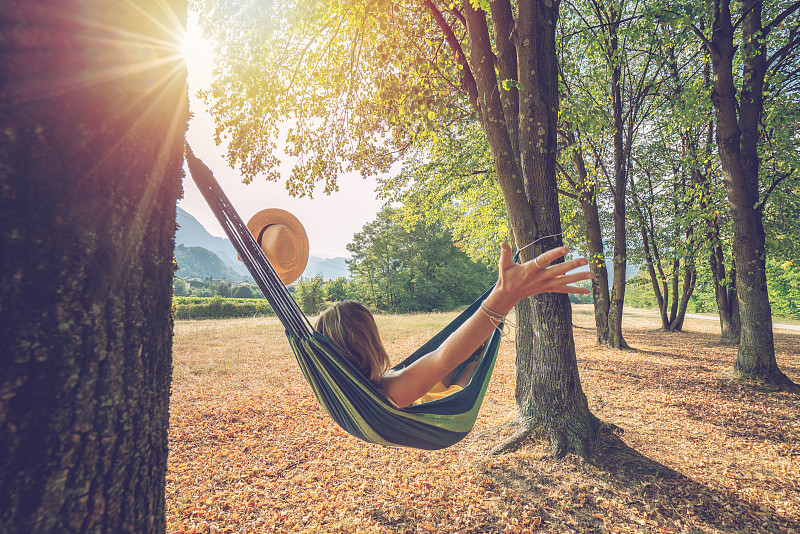 快乐的年轻女子在吊床上放松在秋天-人们旅游度假的自然概念图片素材