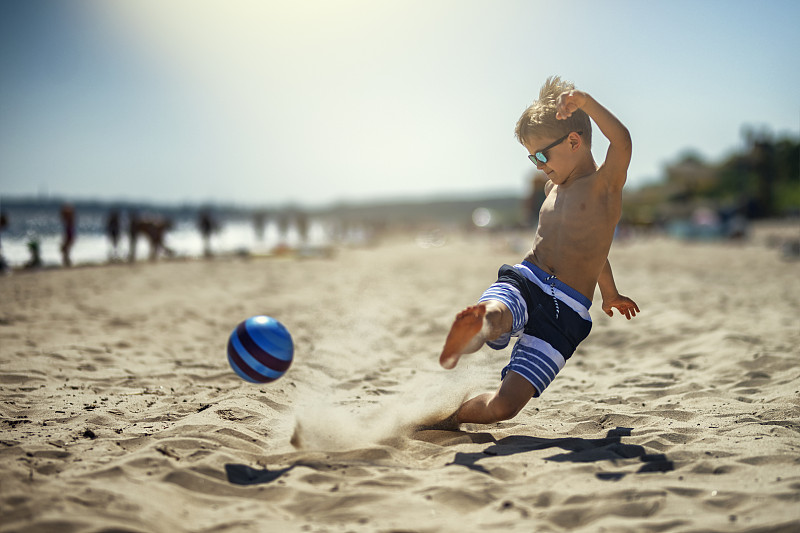 小男孩在沙滩上踢足球图片下载