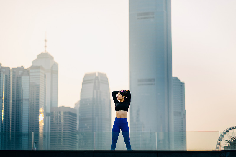 自信和决心的亚洲女运动员伸展双臂在户外对着城市景观日落图片下载