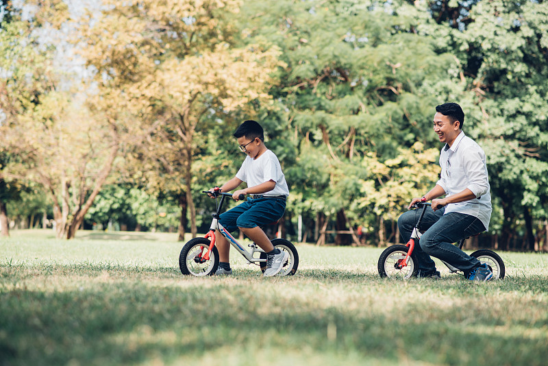 男孩和父亲在草地上骑自行车图片素材
